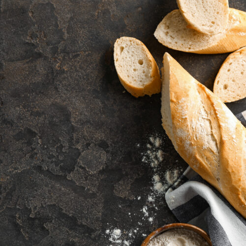 Cut French bread with flour on grey background